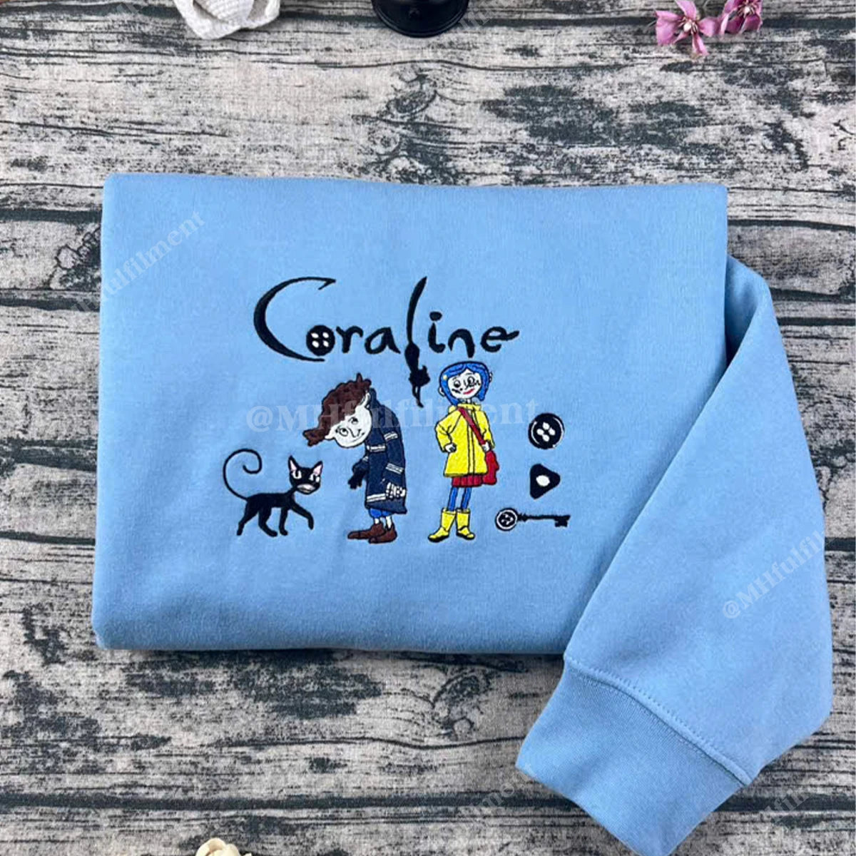 Folded blue sweatshirt with 'Coraline' character design on a wooden surface