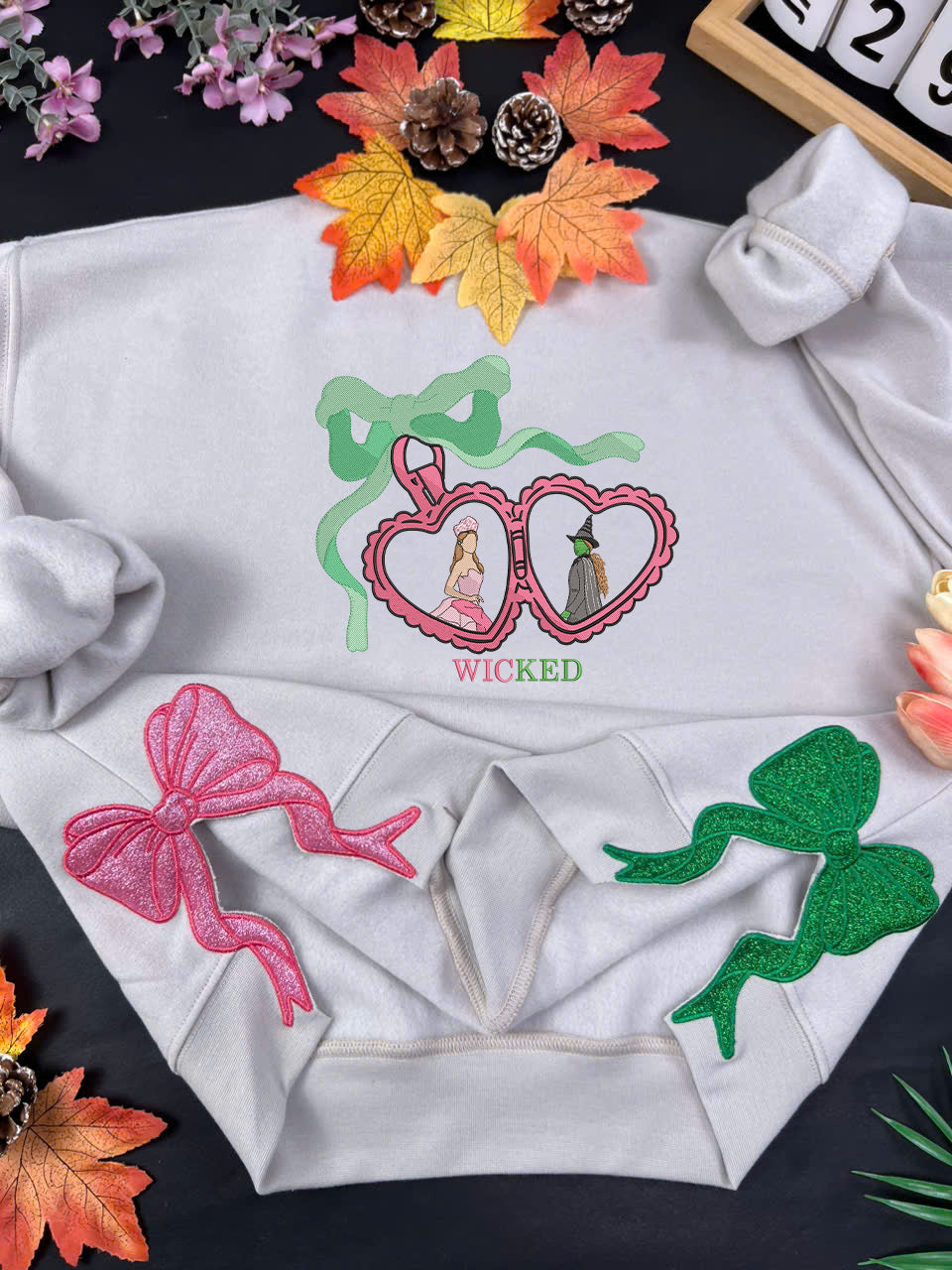 White hoodie with 'Wicked' themed designs on a dark surface with decorative elements.