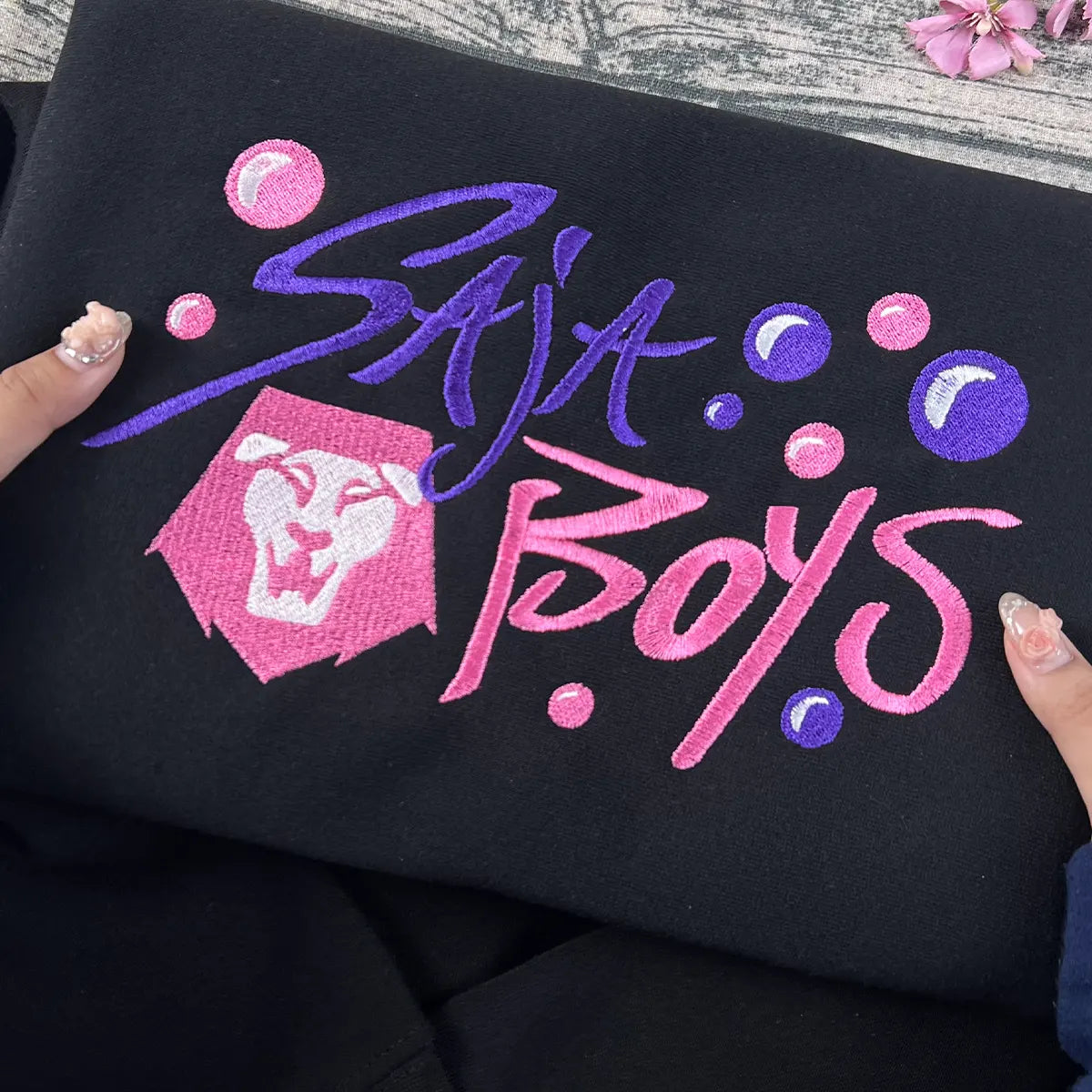 Embroidered design on black fabric with 'Saja Boys' text and pink logo.
