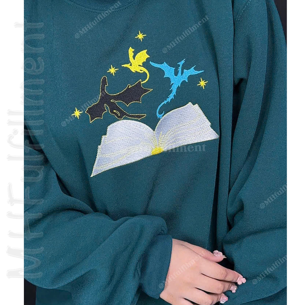 Teal sweatshirt with embroidered design of a book, dragon, and fairy on a white background.