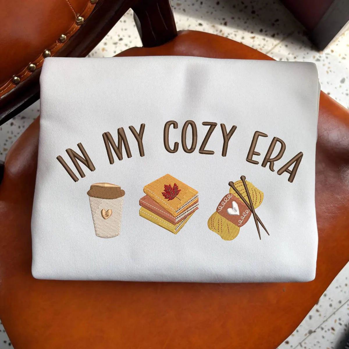 White pouch with 'In My Cozy Era' text and illustrations on a brown surface.