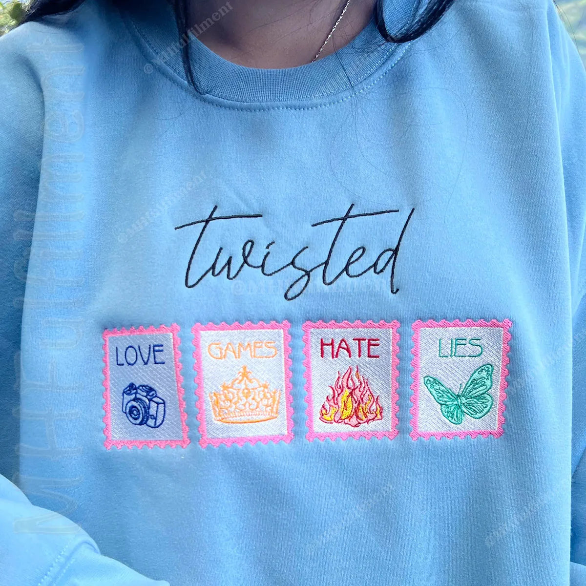 Blue sweatshirt with embroidered text and symbols on a blurred natural background