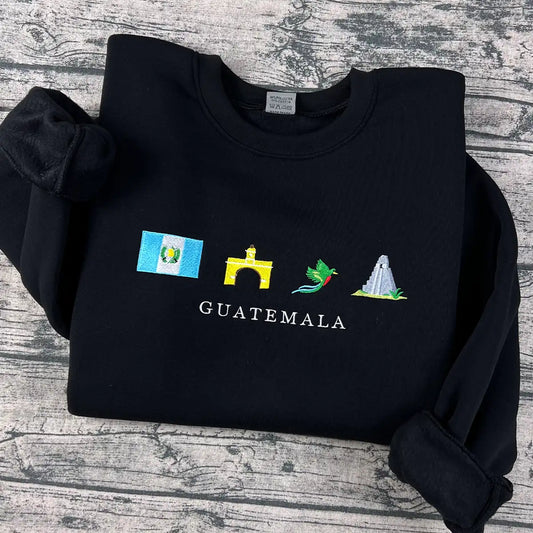 Black sweatshirt with embroidered icons and 'Guatemala' text on a wooden surface