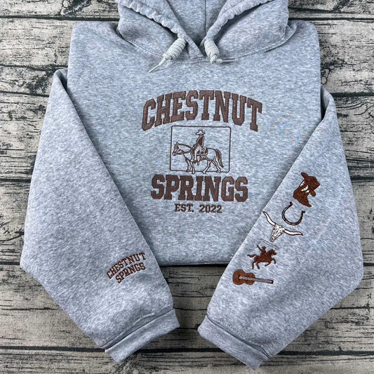 Gray hoodie with 'Chestnut Springs' branding and graphics on a wooden surface