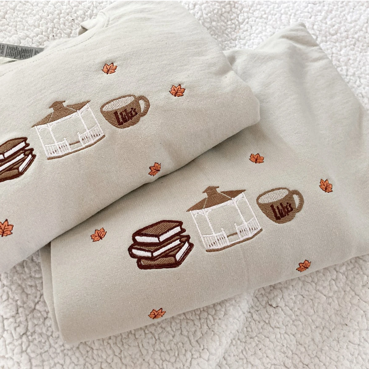 Folded fabric with embroidered designs of a house, cup, and sandwich on a textured surface.