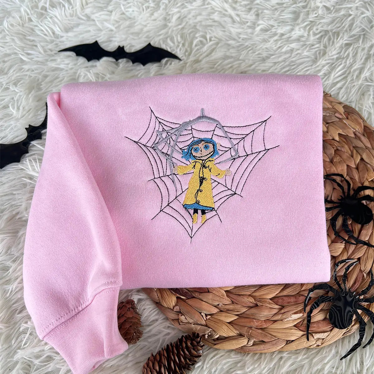 Pink sweatshirt with a spider web and character design on a textured surface with decorative elements.