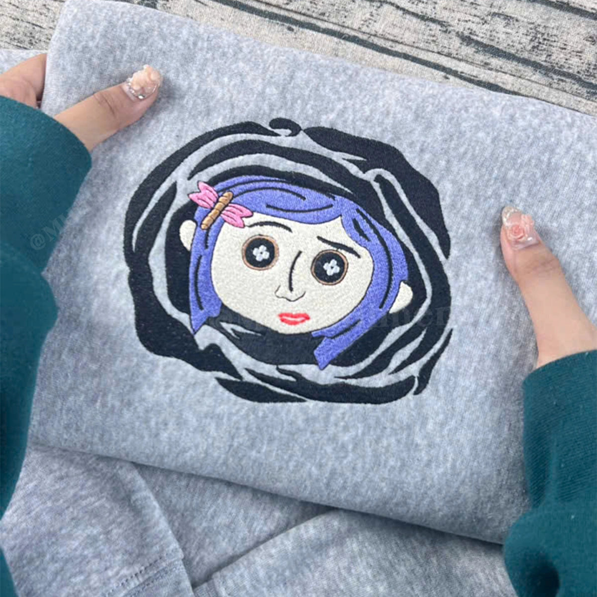 Gray sweatshirt with an embroidered design of a character with blue hair and a pink bow.