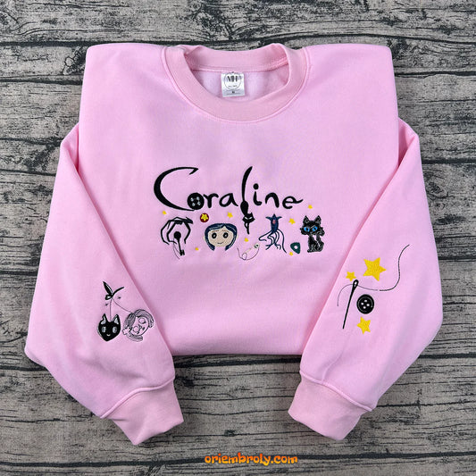 Pink sweatshirt with character designs and 'Coraline' text on a wooden surface