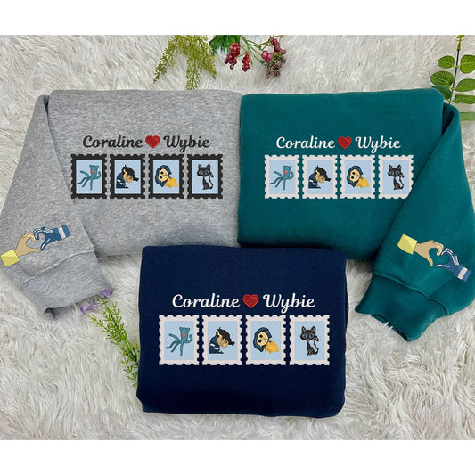 Three sweatshirts in gray, blue, and green with 'Coraline Wybie' design on a textured surface.