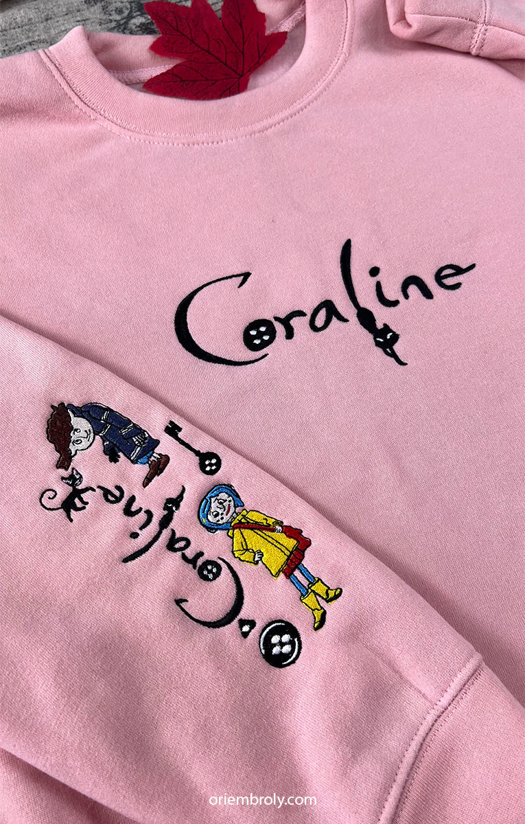 Pink sweatshirt with 'Coraline' characters and text on a plain background