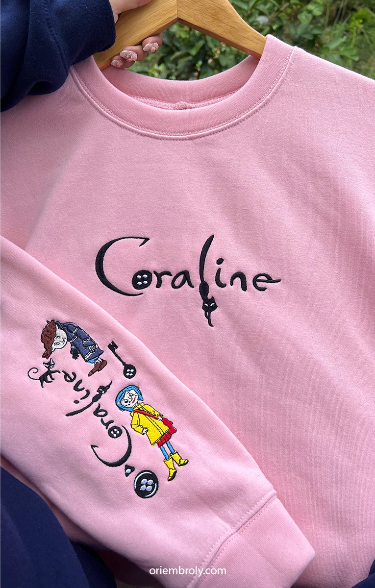 Pink sweatshirt with 'Coraline' design and characters on a hanger.