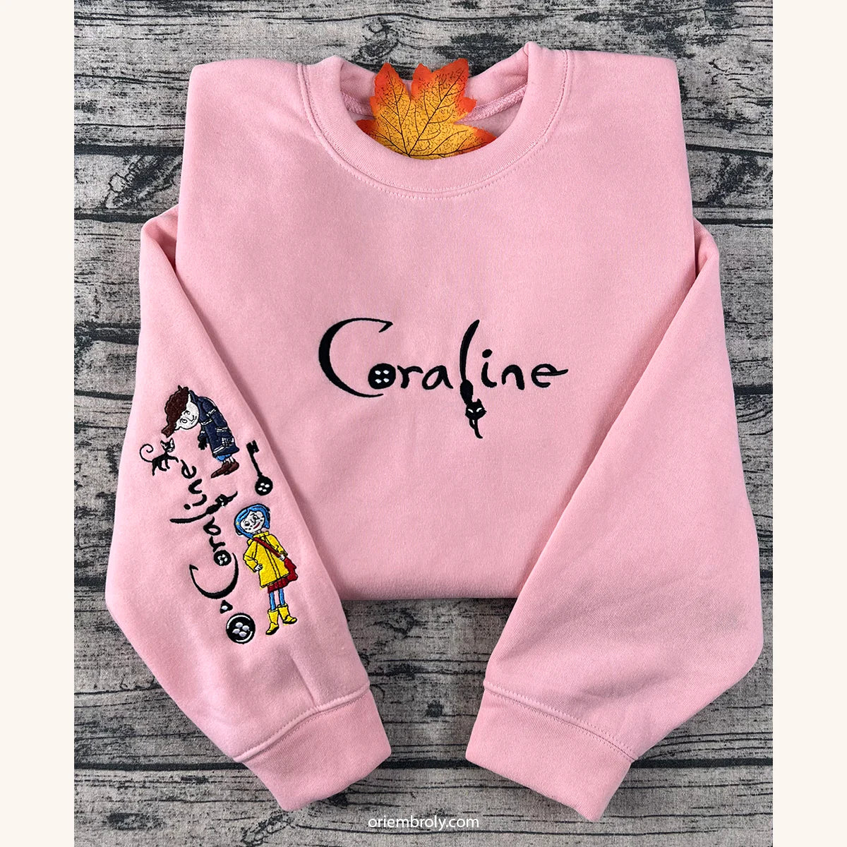 Pink sweatshirt with 'Coraline' design on a wooden surface