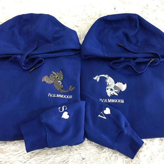 Two blue hoodies with embroidered designs on a textured surface