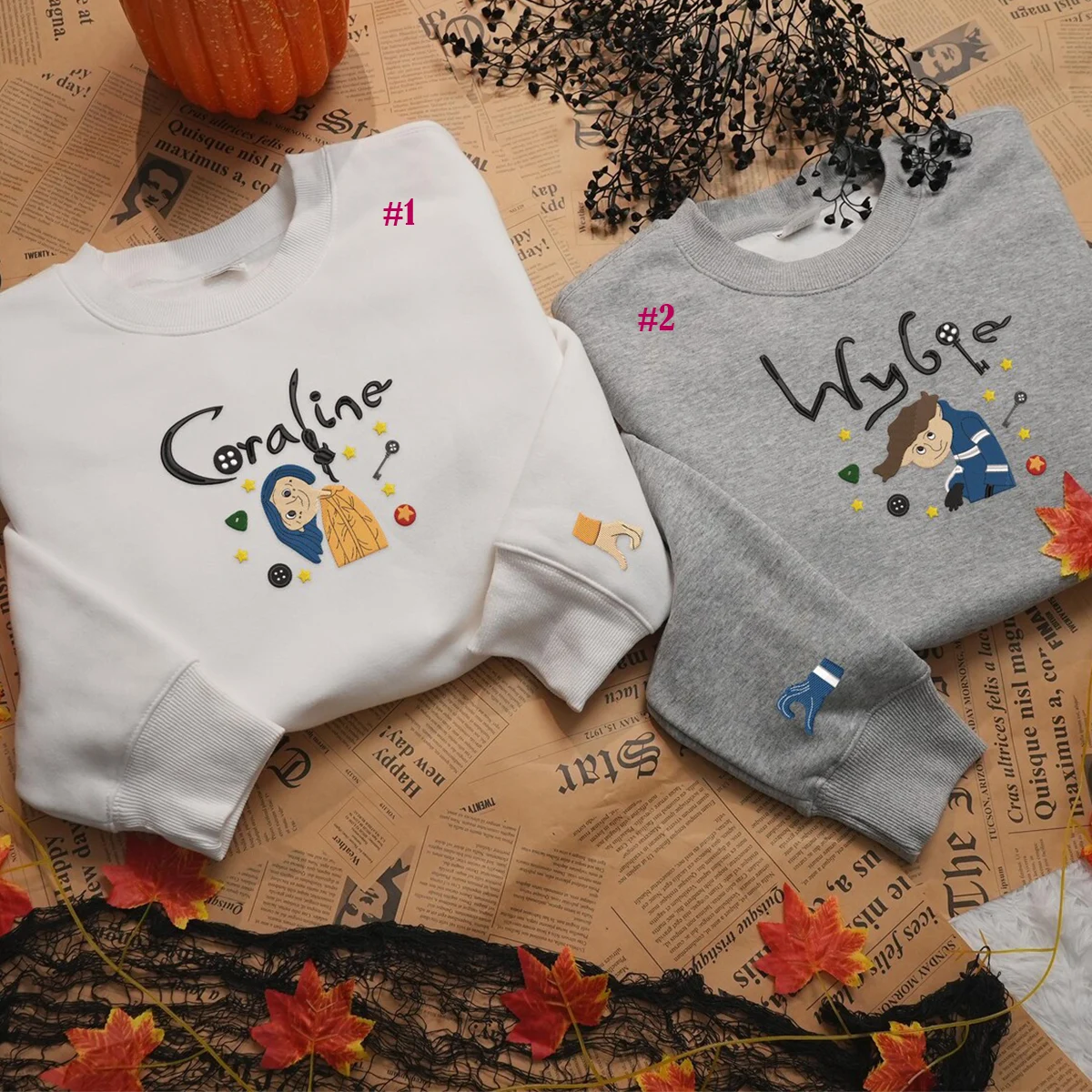Two sweatshirts, one white and one gray, with embroidered designs on a newspaper background.
