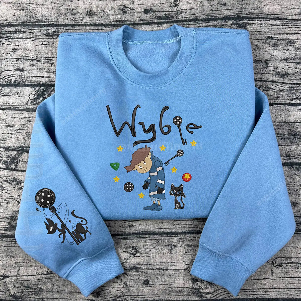 Light blue sweatshirt with cartoon character and 'Wybie' text on a wooden surface