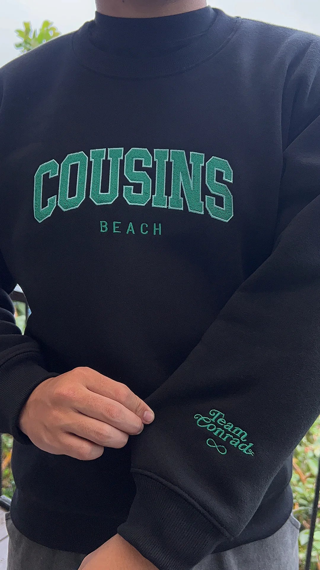 Black sweatshirt with 'Cousins Beach' text and 'Team Conrad' embroidery.