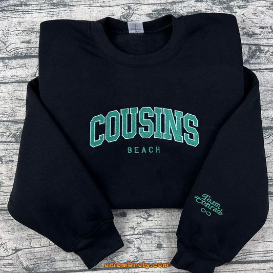 Black sweatshirt with 'Cousins Beach' text on a wooden surface