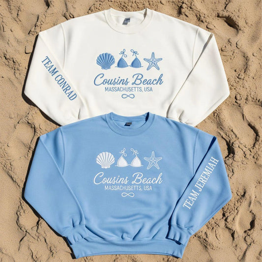 Two sweatshirts with beach-themed designs on a sandy background