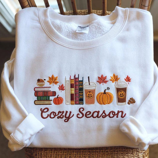 White sweatshirt with autumn-themed design and 'Cozy Season' text on a chair.
