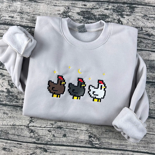 White sweatshirt with pixelated chicken designs on a wooden surface