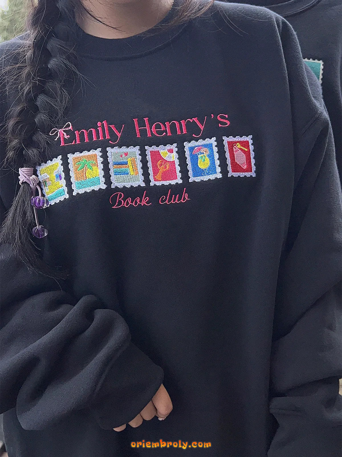 Black sweatshirt with colorful text and graphics, featuring 'Emily Henry's Book Club' on a blurred background.
