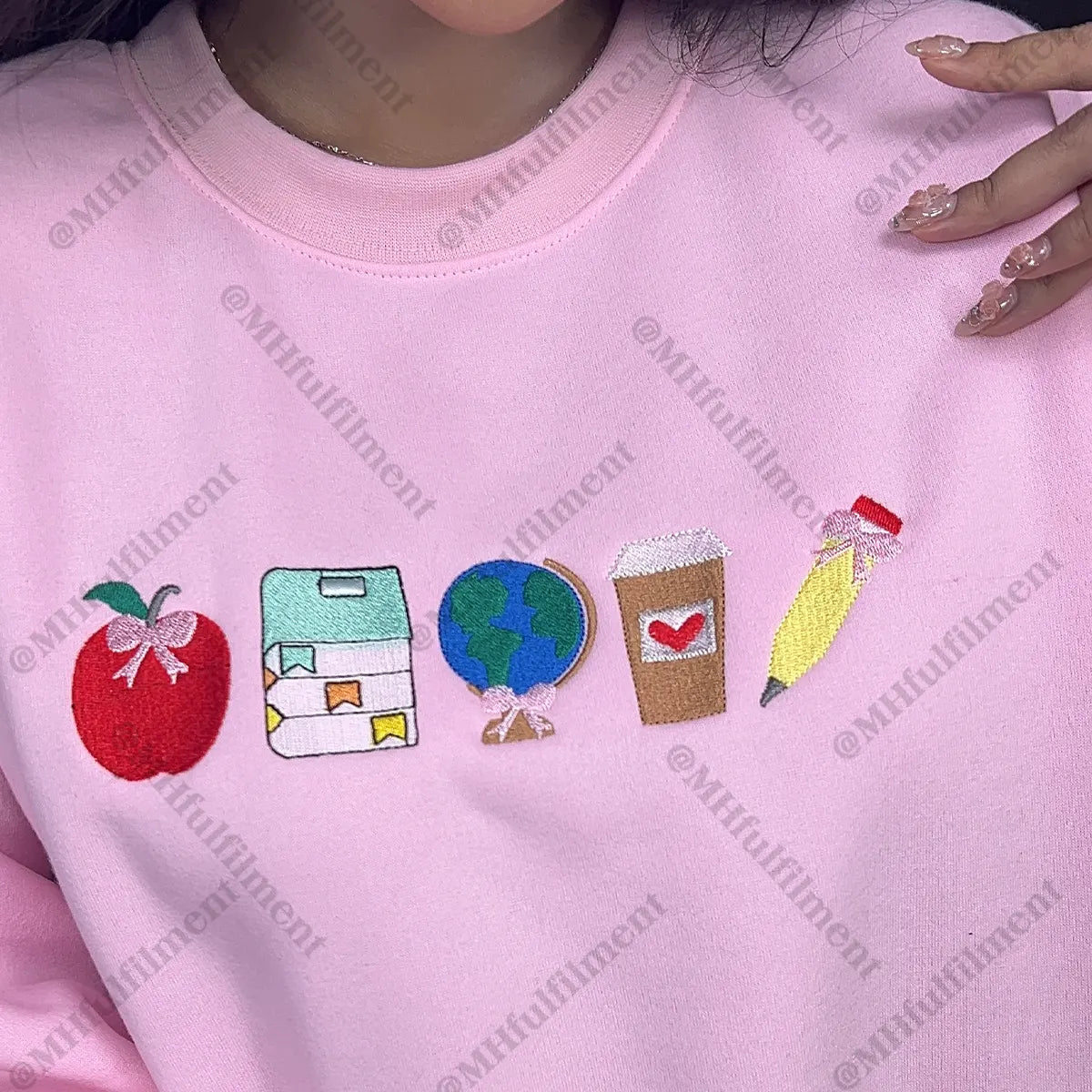 Pink sweatshirt with embroidered icons including an apple, house, globe, coffee cup, and pen.