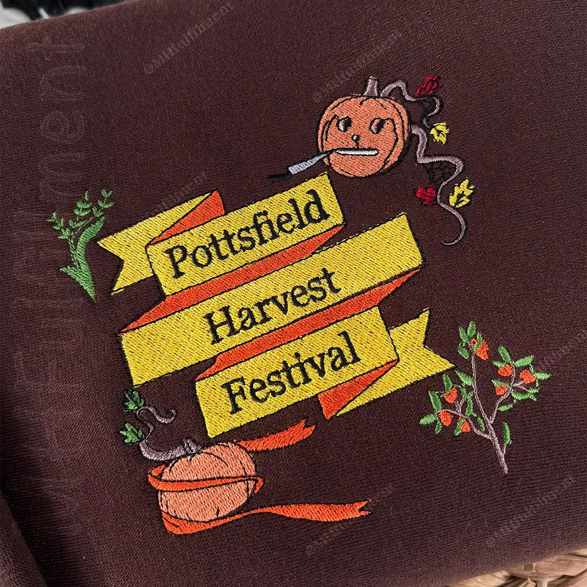 Embroidered design of a pumpkin with text 'Pottsfield Harvest Festival' on a brown fabric background.