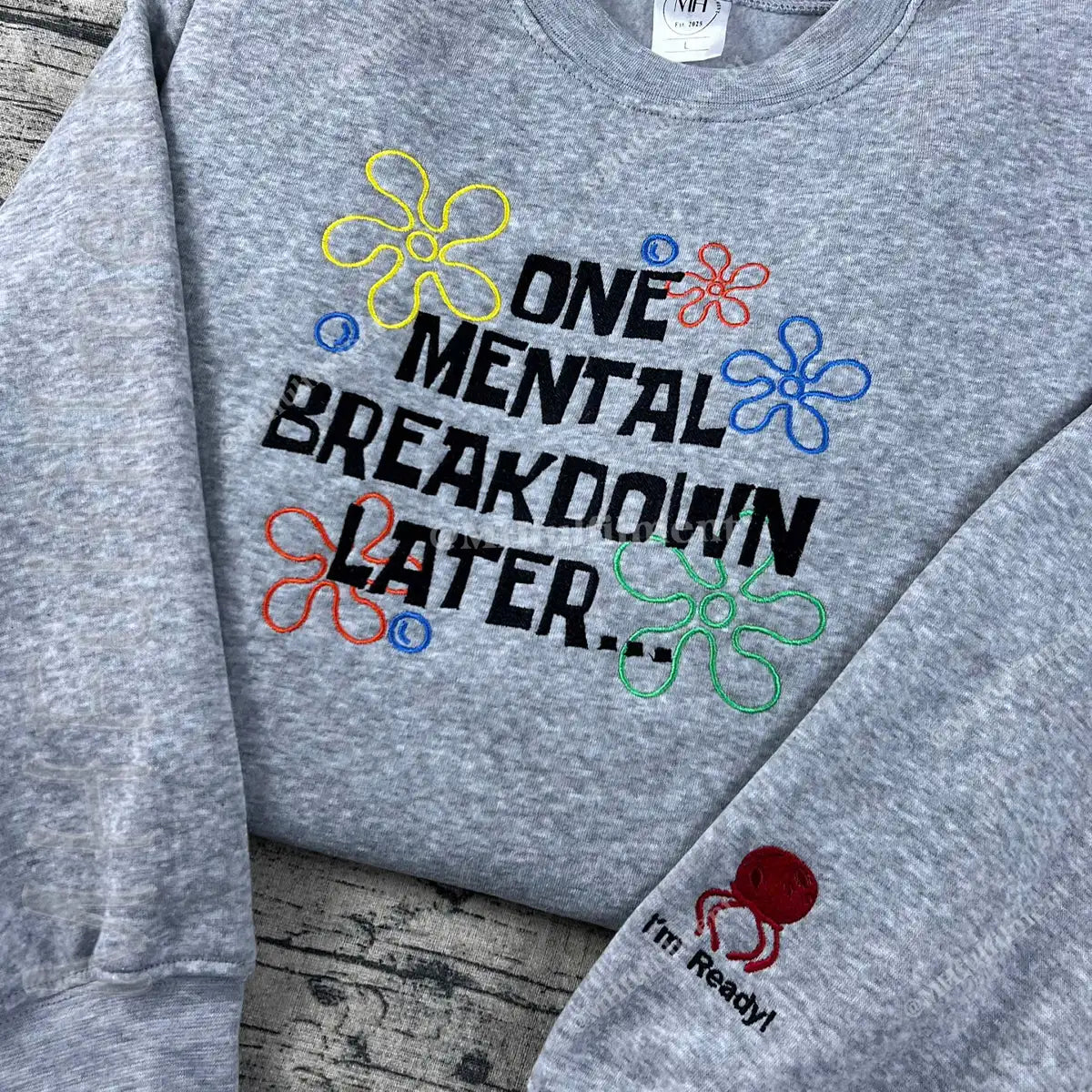 Gray sweatshirt with colorful text and flower graphics on a wooden surface
