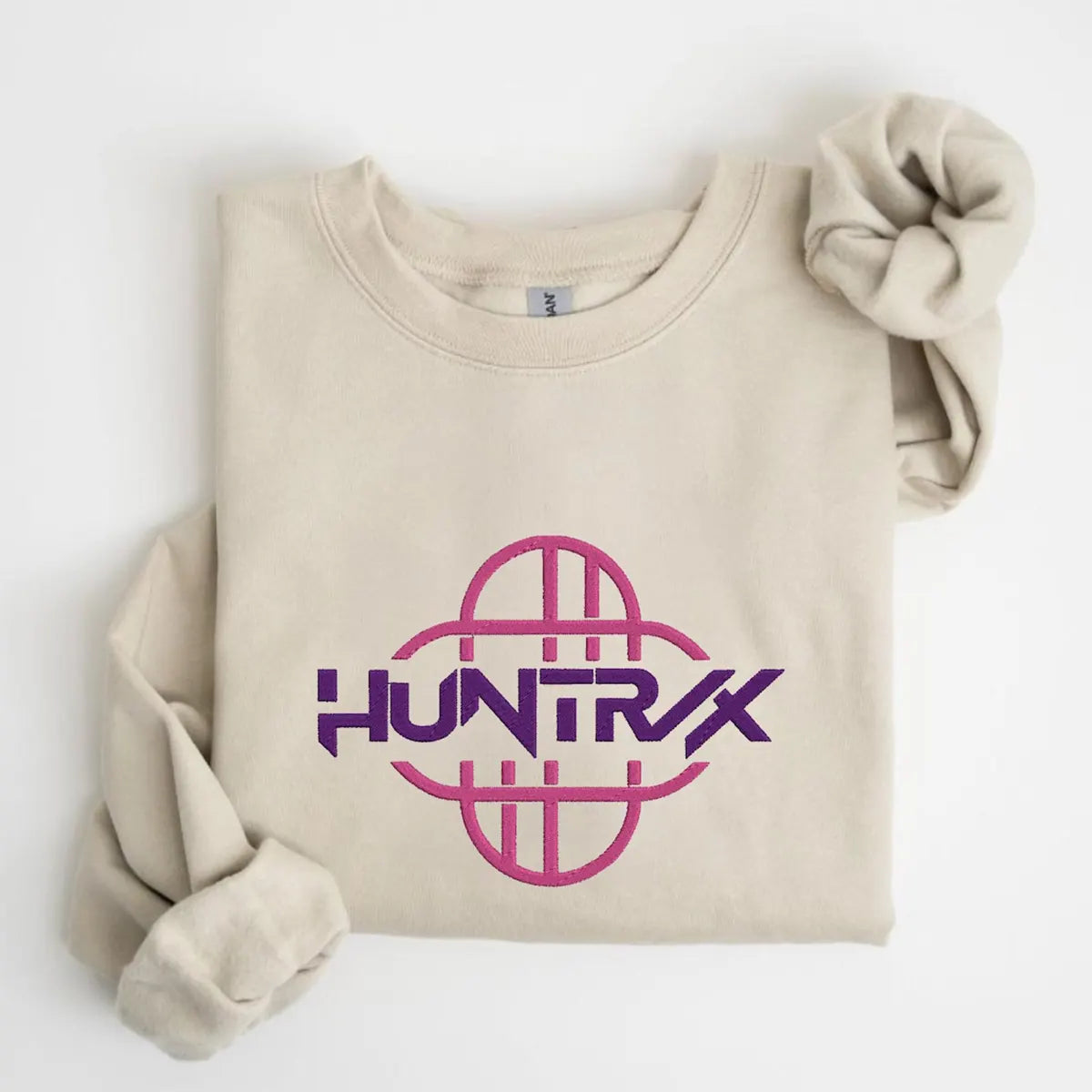 Beige sweatshirt with pink 'HUNTRX' logo on a white background