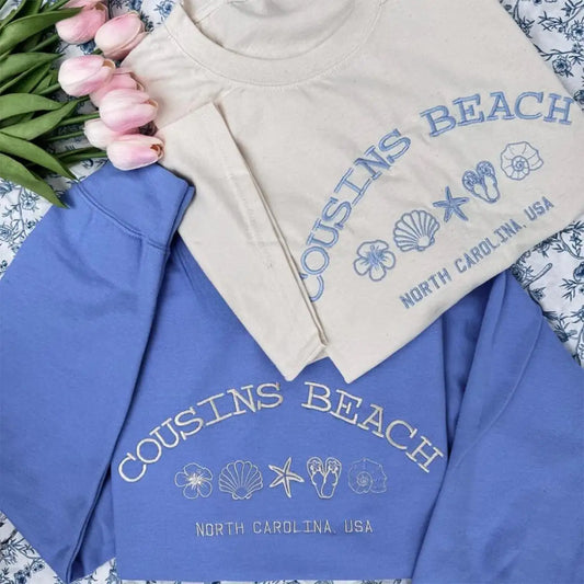 Two sweatshirts with 'Cousins Beach' text and beach-themed graphics on a patterned surface.