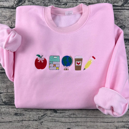 Pink sweatshirt with colorful embroidered icons on a wooden surface