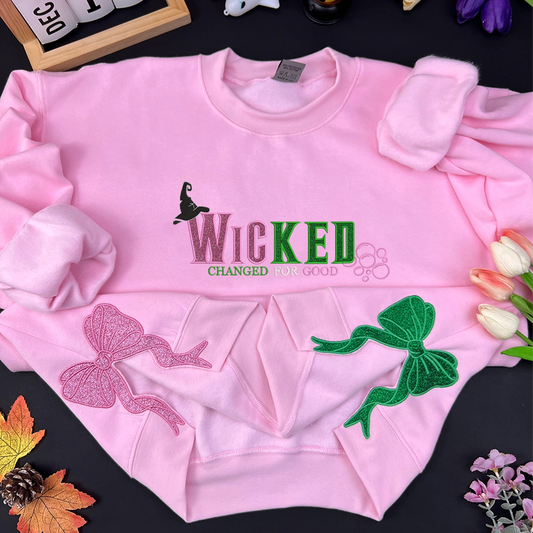 Pink sweatshirt with 'WICKED CHANGED FOR GOOD' text and decorative elements on a black background.