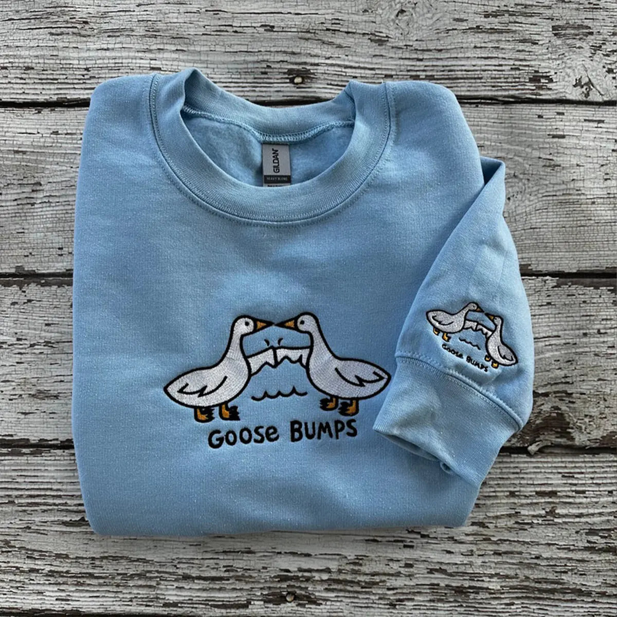 Light blue sweatshirt with goose design and 'Goose Bumps' text on a wooden surface