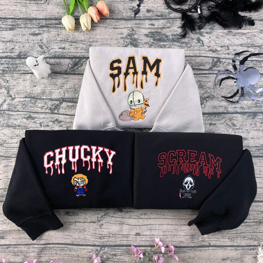 Two hoodies with embroidered text and graphics on a wooden surface with decorative items.