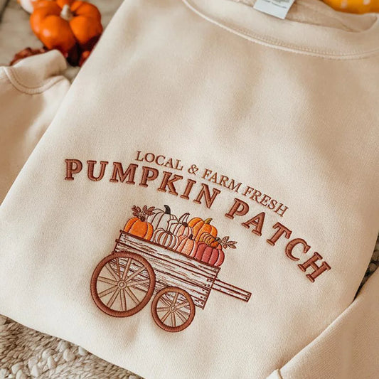 Beige sweatshirt with 'Local & Farm Fresh Pumpkin Patch' text and pumpkin design on a textured surface.