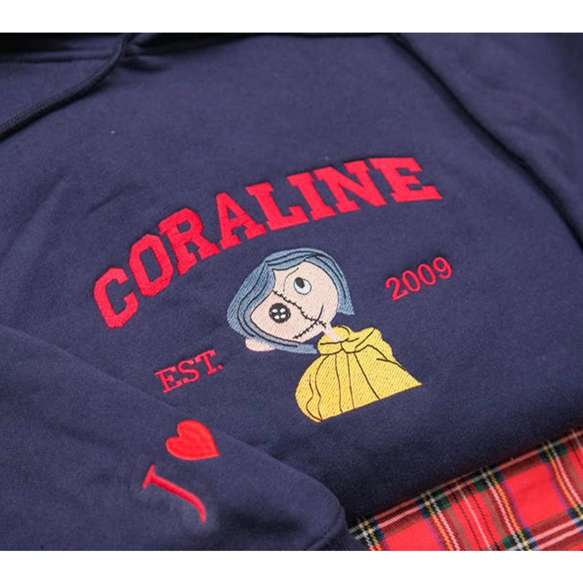 Navy blue hoodie with 'Coraline' design and text on a plaid fabric background
