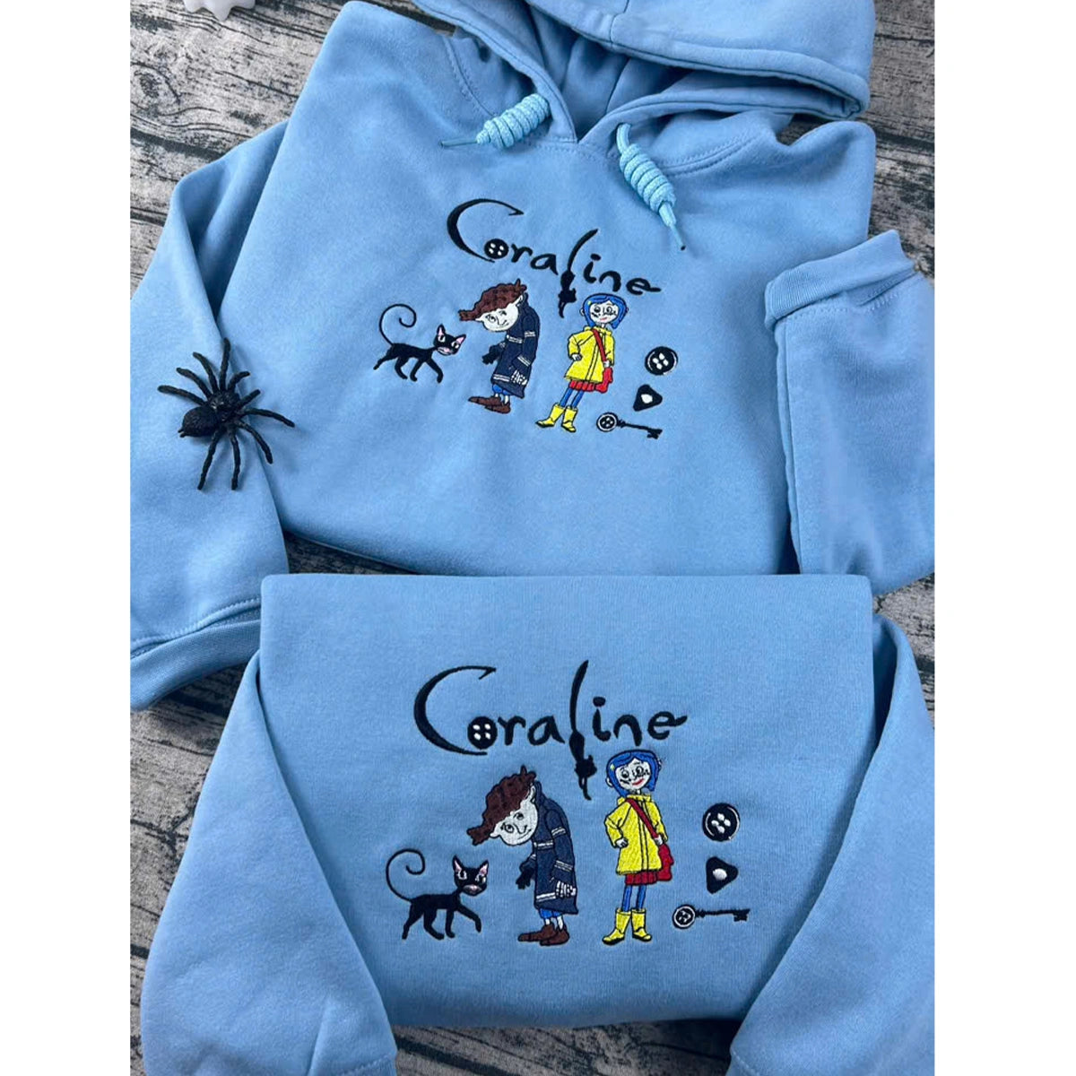 Light blue hoodie with 'Coraline' character design on a wooden surface