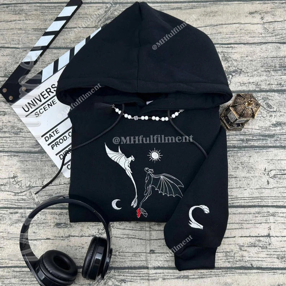 Black hoodie with bat design on a wooden surface with headphones and clapperboard.