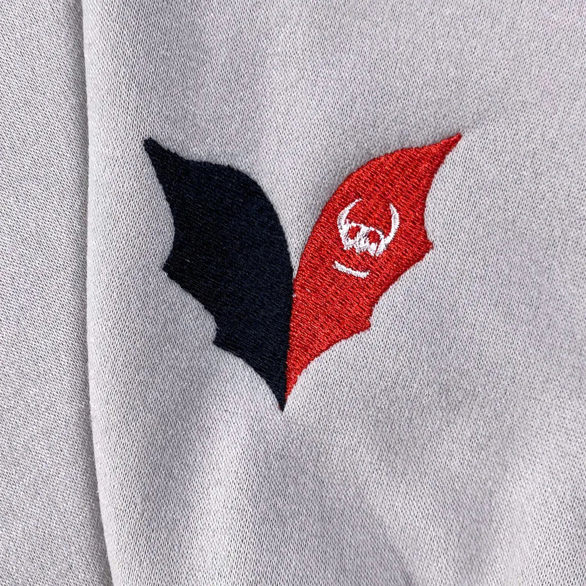 Two embroidered shapes on a gray background, one black and one red with a white symbol.
