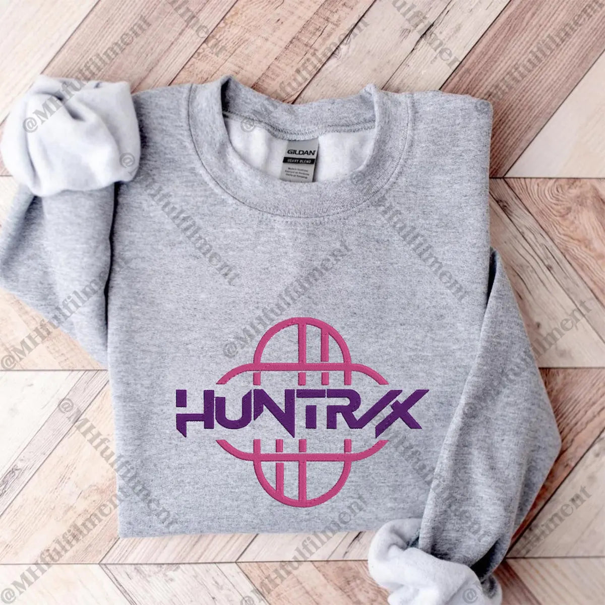 Gray sweatshirt with pink and purple 'HUNTRX' logo on a wooden floor