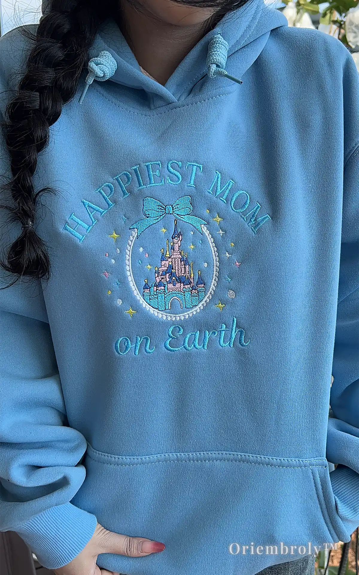 Light blue embroidered hoodie with a whimsical "Happiest Mom on Earth" design. Features sparkling stars and a princess castle, capturing the magical mom lifestyle for everyday wear