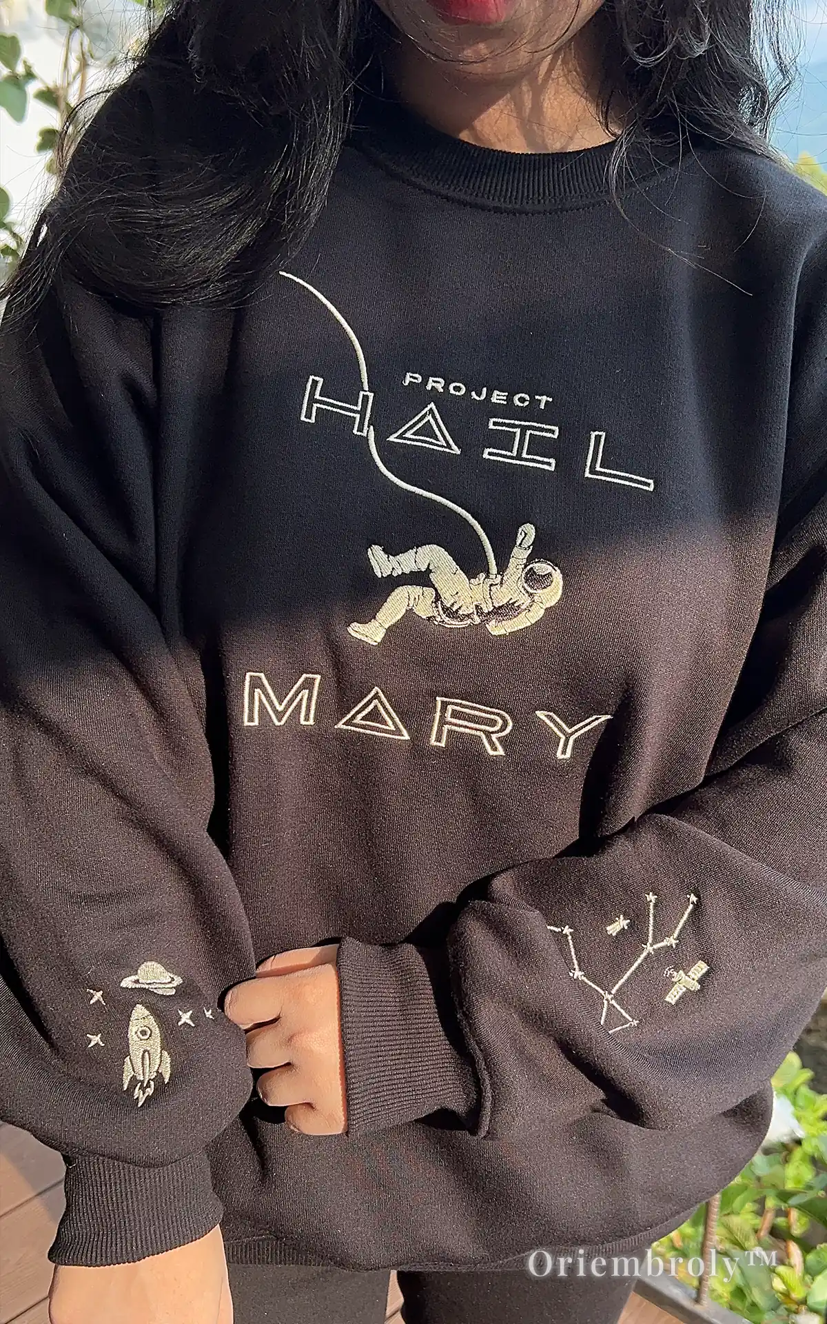 Minimalist sci-fi streetwear: black crewneck with detailed astronaut and cosmic sleeve embroidery. Narrative-driven apparel inspired by modern literature and outer space exploration, perfect for a clean, aesthetic look