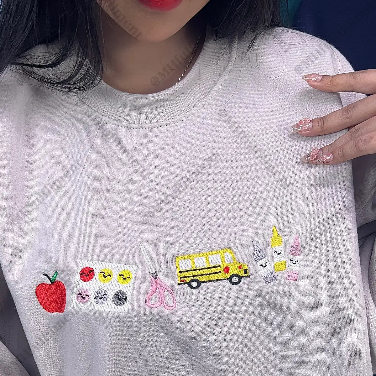 White sweatshirt with various embroidered designs including an apple, scissors, a school bus, and more.