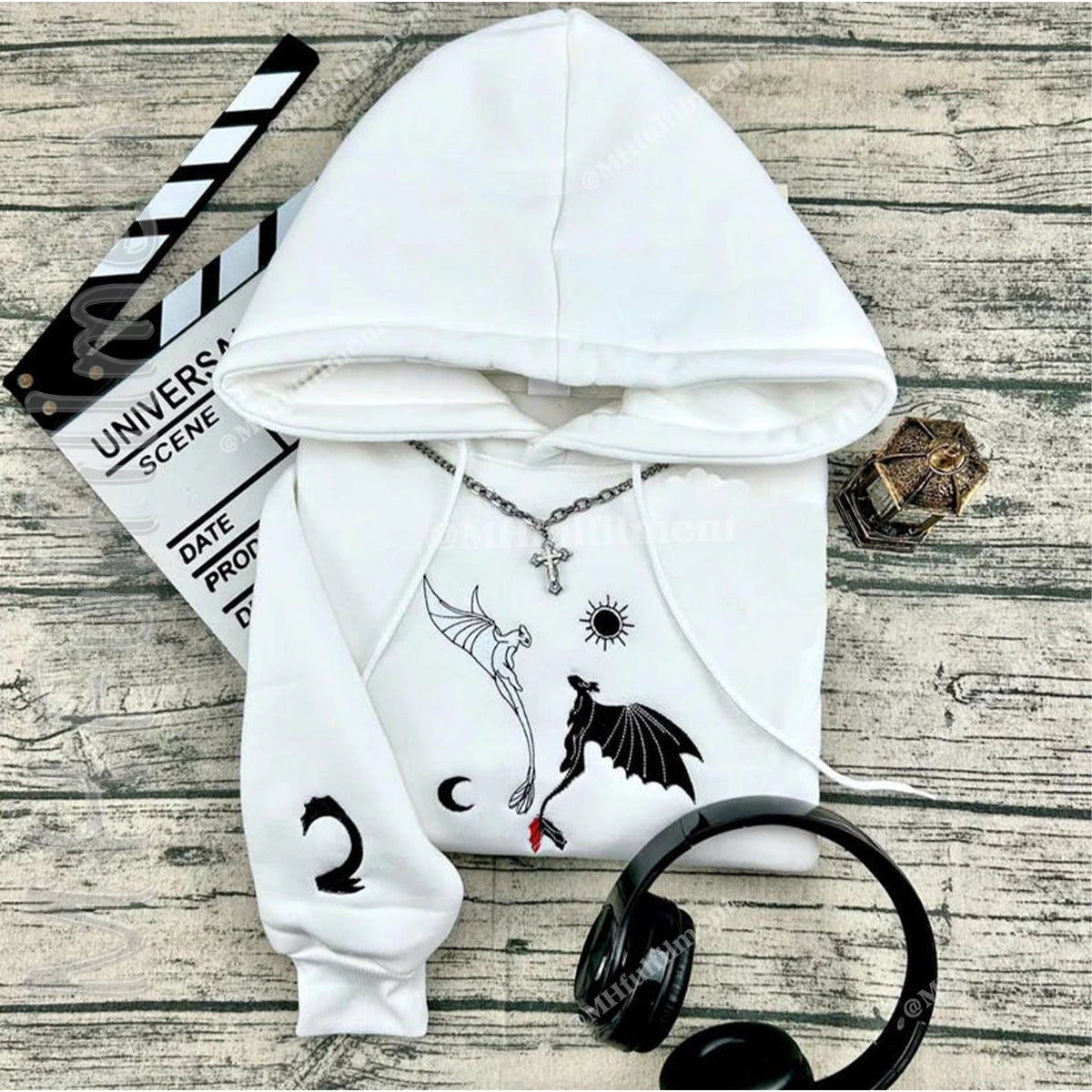 White hoodie with black designs on a wooden surface with headphones and a clapboard.