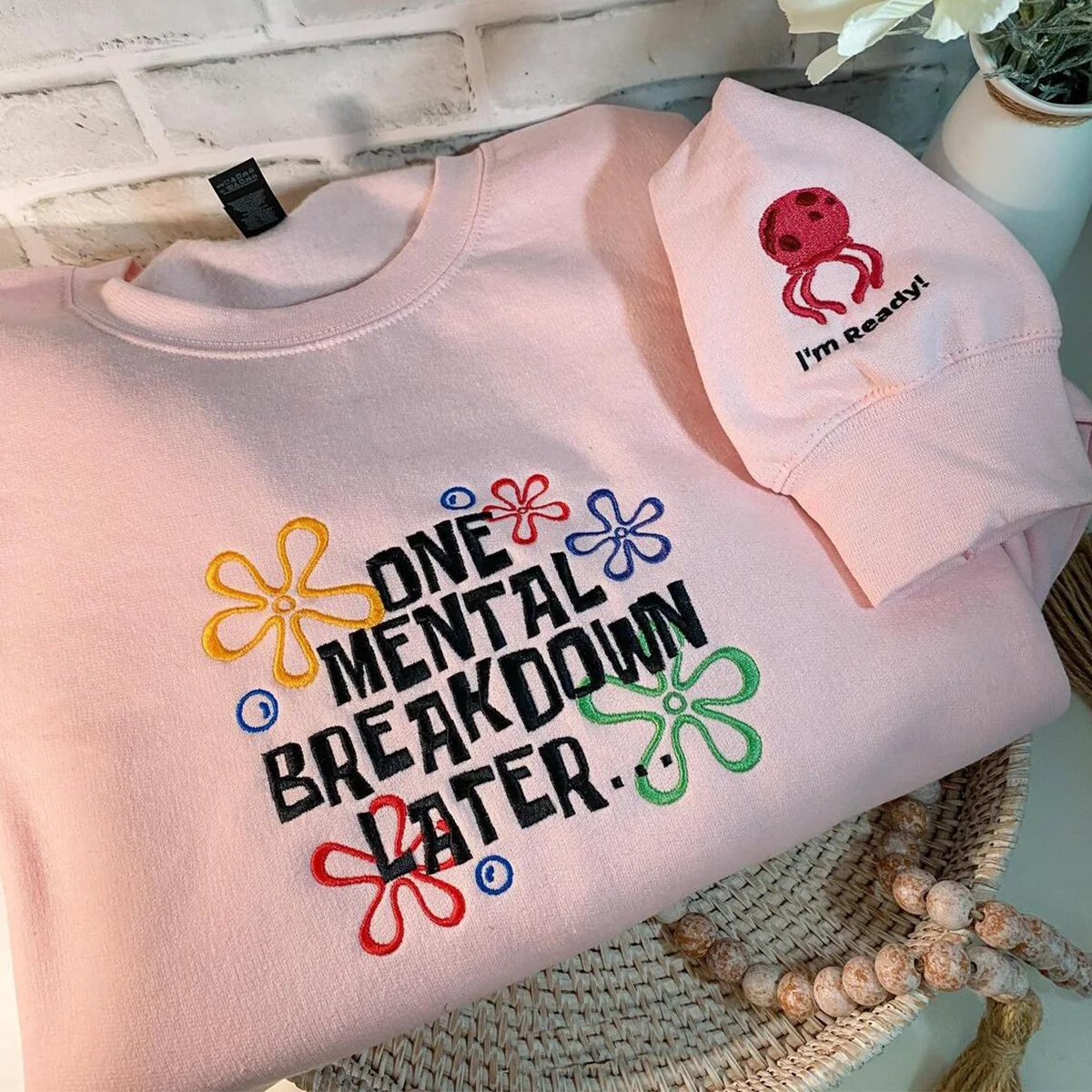 Pink sweatshirt with colorful text and flower designs on a textured surface.