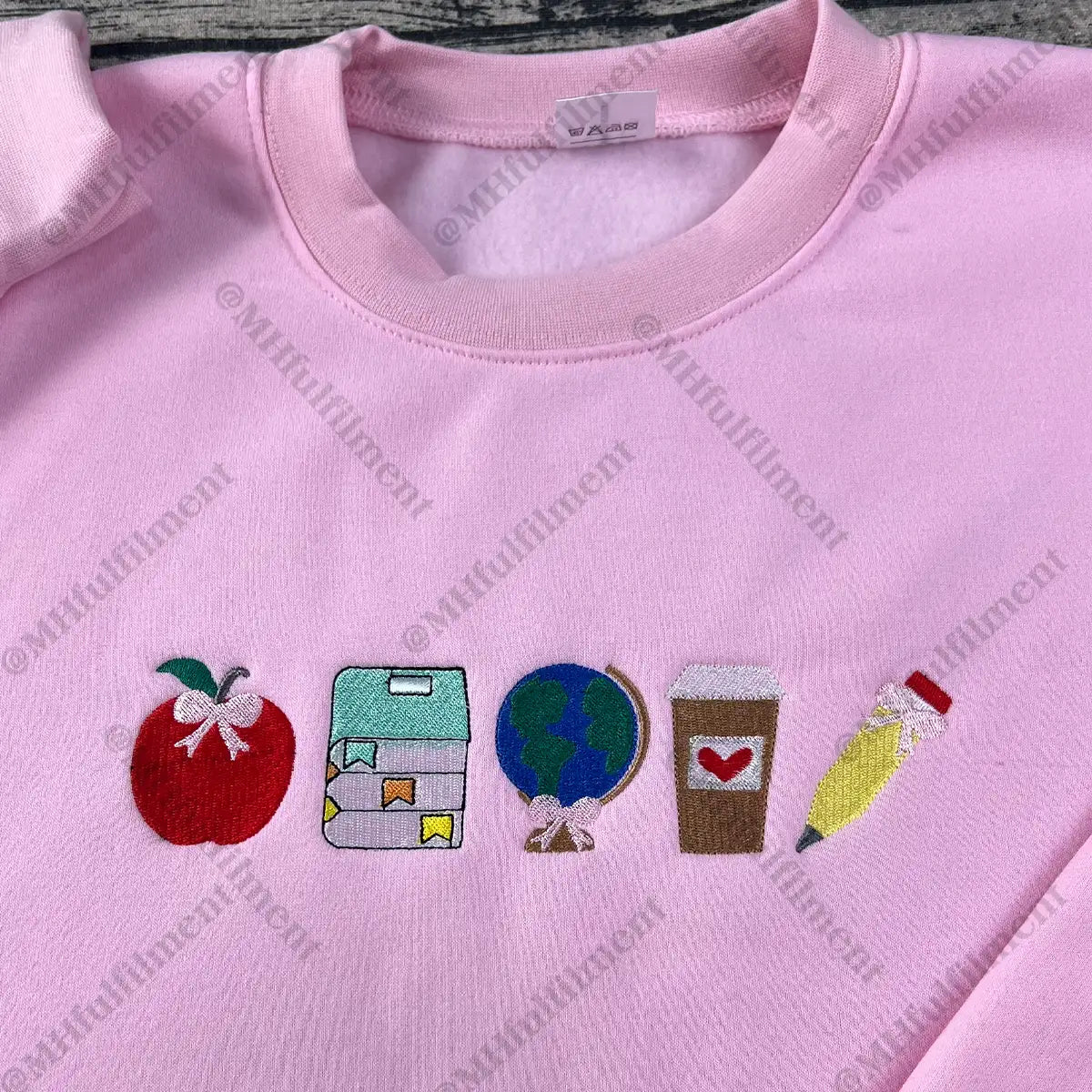 Pink sweatshirt with embroidered icons including an apple, book, world, coffee cup, and pencil.