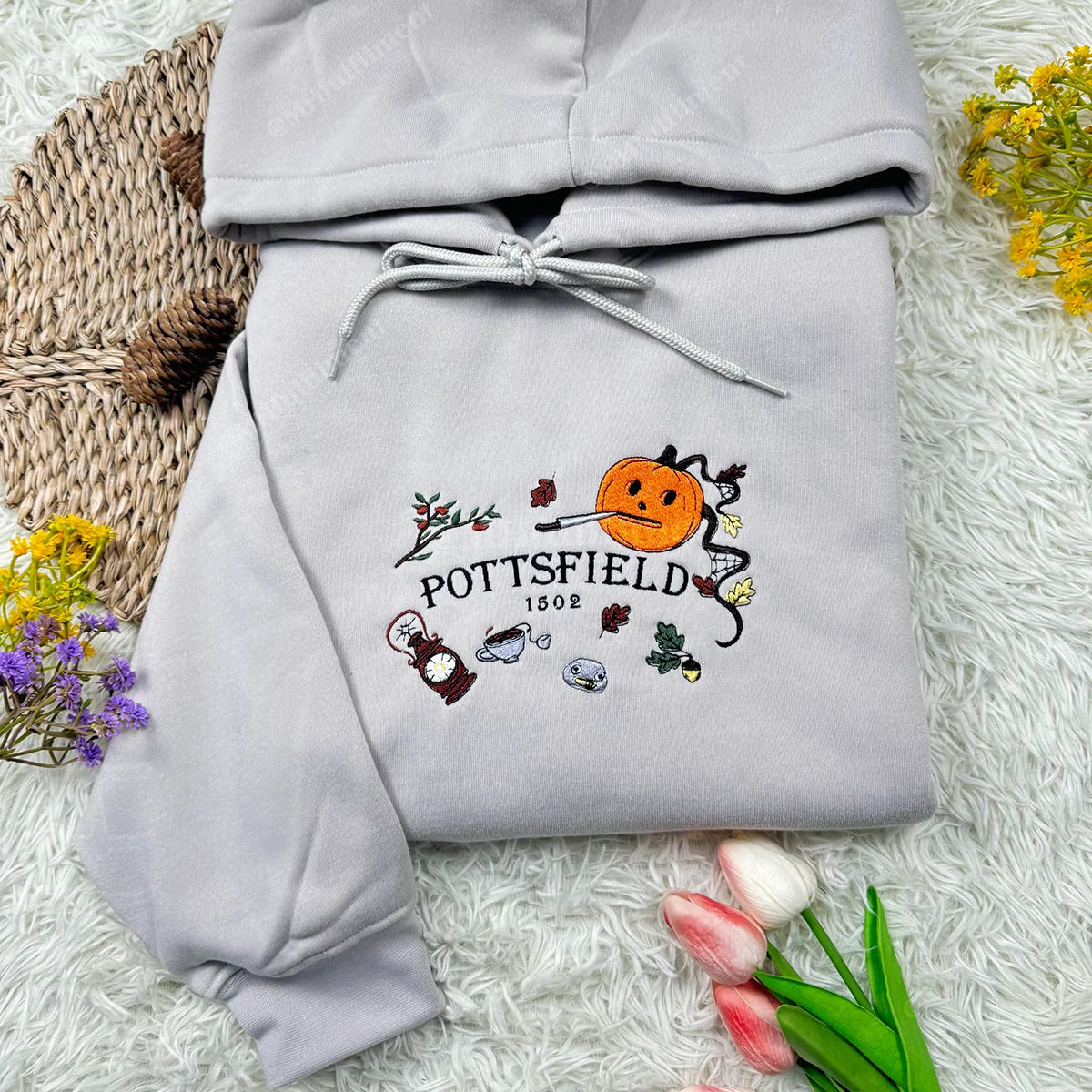 Gray hoodie with embroidered design on a textured surface with flowers.