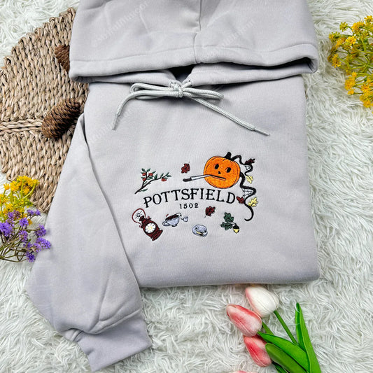 Gray hoodie with embroidered design on a textured surface with flowers.