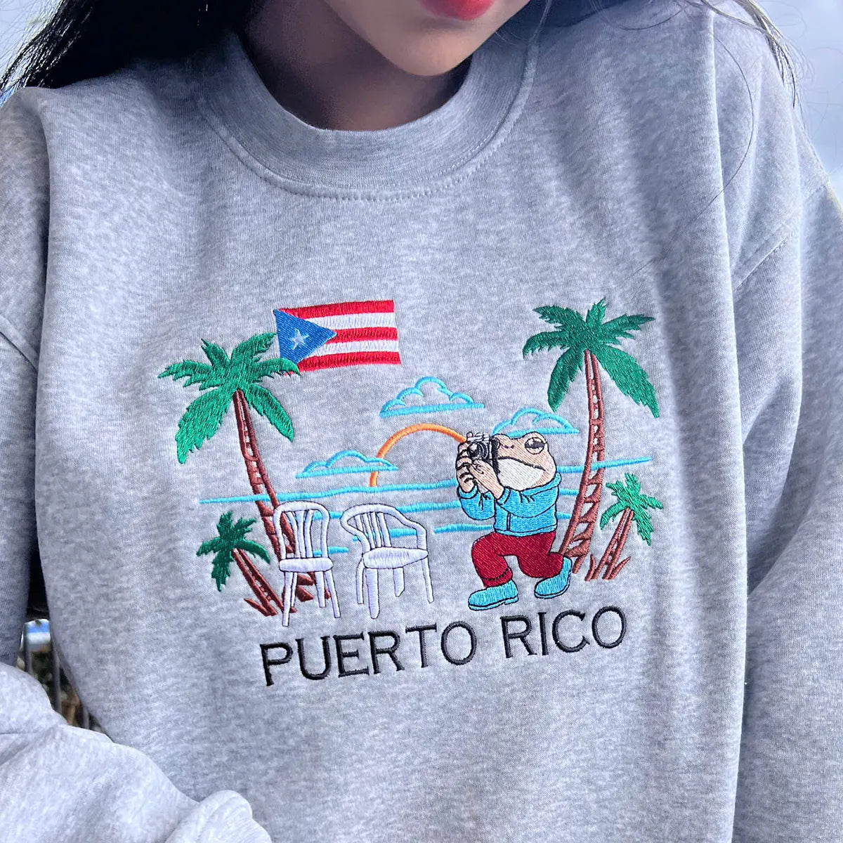 Gray sweatshirt with a Puerto Rican flag and tropical design on a person.