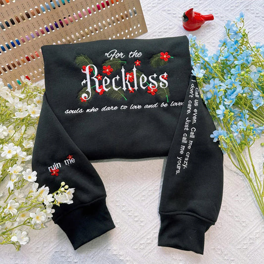 Black sweatshirt with floral designs and text on a textured surface with flowers.